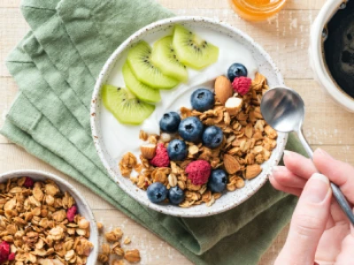 Café da manhã posto. Na imagem vemos uma xícara de café preto, tigela com iogurte, cereal e frutas, mel e outra tigela com granola.