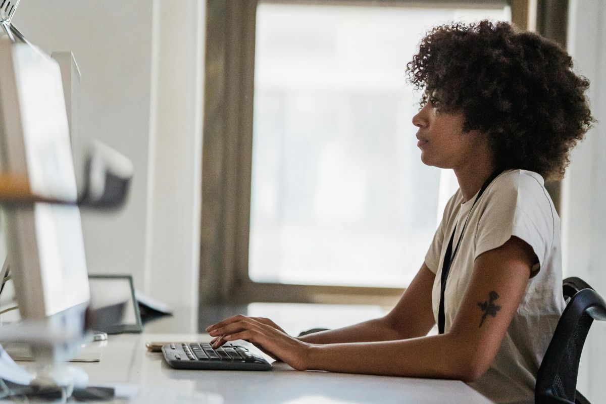  Uma mulher, sentada em frente ao computador em seu escritório, trabalha concentrada, representando a energia e o foco que podem ser otimizados com o uso de multivitaminicos.