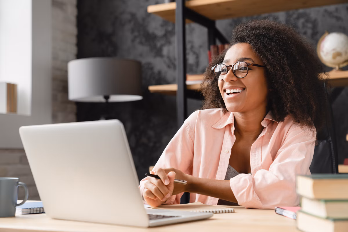 Jovem mulher sorridente, sentada no escritório em casa, trabalhando em seu notebook.