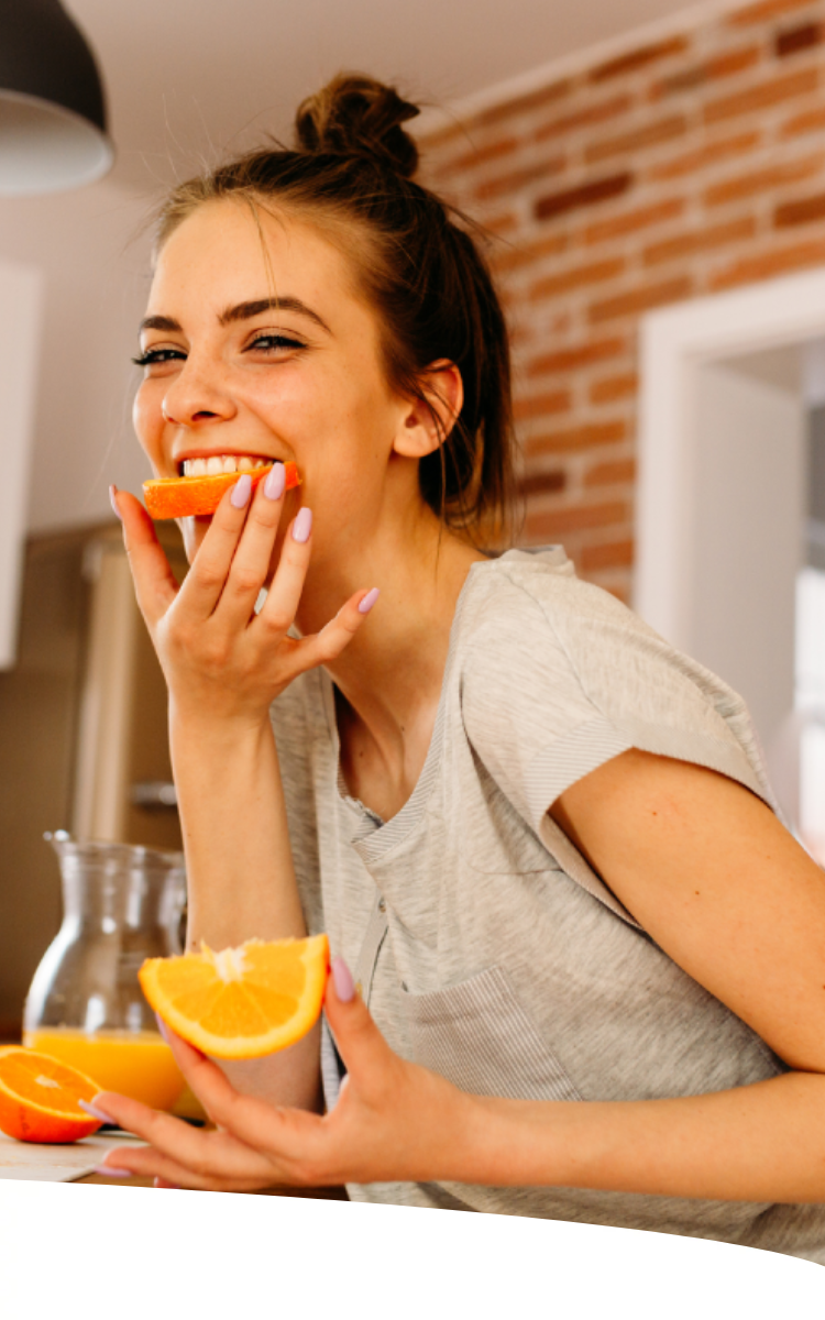 Mulher sorridente comendo metade de uma rodela de laranja.