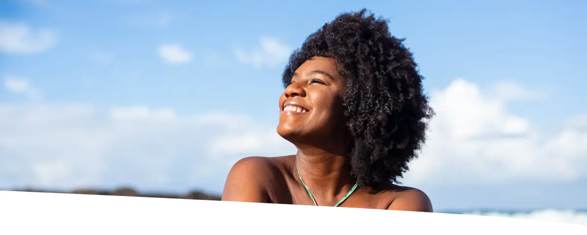 Mulher sentada em pedras, em uma linda praia, em dia ensolarado.