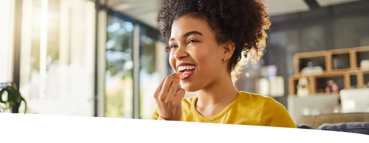 Mulher sorrindo enquanto toma um suplemento e segura um copo d’água, ilustrando o uso da arginina no dia a dia para mais disposição.