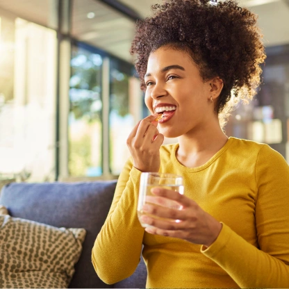 Mulher sorrindo enquanto toma um suplemento e segura um copo d’água, ilustrando o uso da arginina no dia a dia para mais disposição.