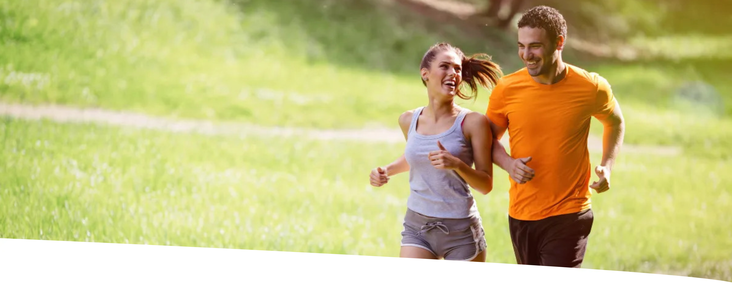 Casal correndo em um parque, sorridente e com aparência saudável. Ambos usam roupas esportivas e praticam atividade física ao ar livre, representando um estilo de vida ativo com energia e bem-estar.