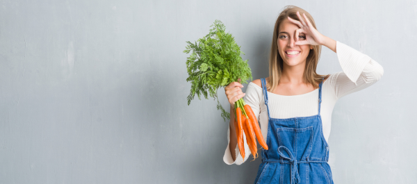 Mulher segurando cenouras pelo talo e destacando o olho com os dedos da outra mão