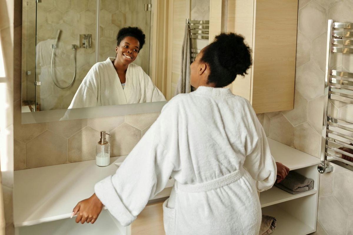 Uma mulher sorri para si mesma no espelho, refletindo a autoestima e o bem-estar que são parte essencial de uma rotina de autocuidado