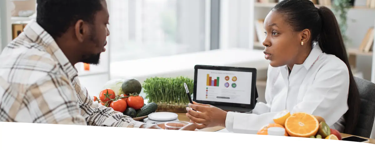 Homem conversando com sua nutricionista. Sobre a mesa, vemos alimentos frescos e suplementos.