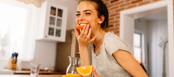 Mulher sorridente comendo metade de uma rodela de laranja.
