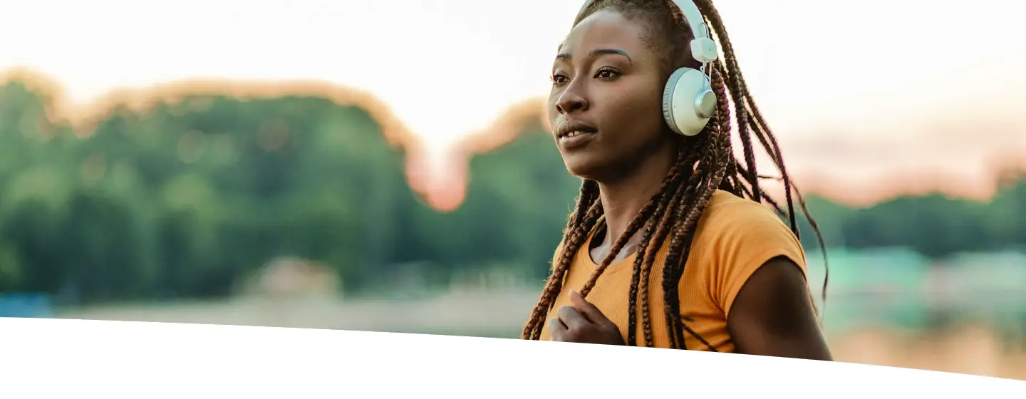 Mulher correndo ao ar livre usando fones de ouvido, representando energia, disposição e bem-estar associados a nutrientes como vitamina C e arginina.