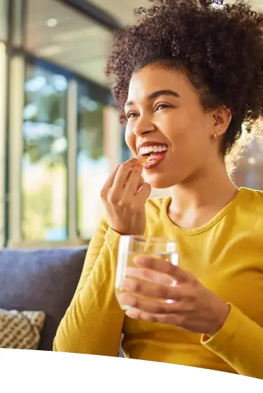 Mulher sorrindo enquanto toma um suplemento e segura um copo d’água, ilustrando o uso da arginina no dia a dia para mais disposição.