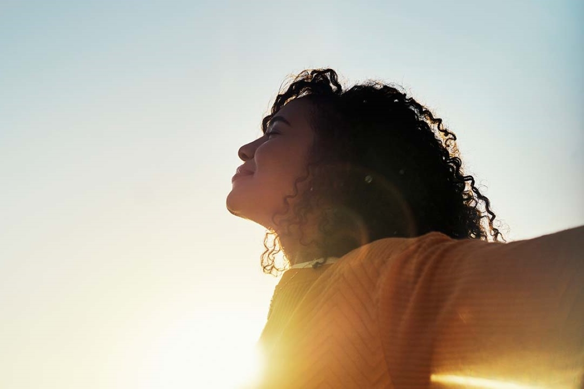 Mulher com expressão de alívio e bem-estar ao ar livre, aproveitando a luz do sol. Imagem transmite leveza e saúde, representando os benefícios de hábitos saudáveis no alívio dos sintomas da TPM.
