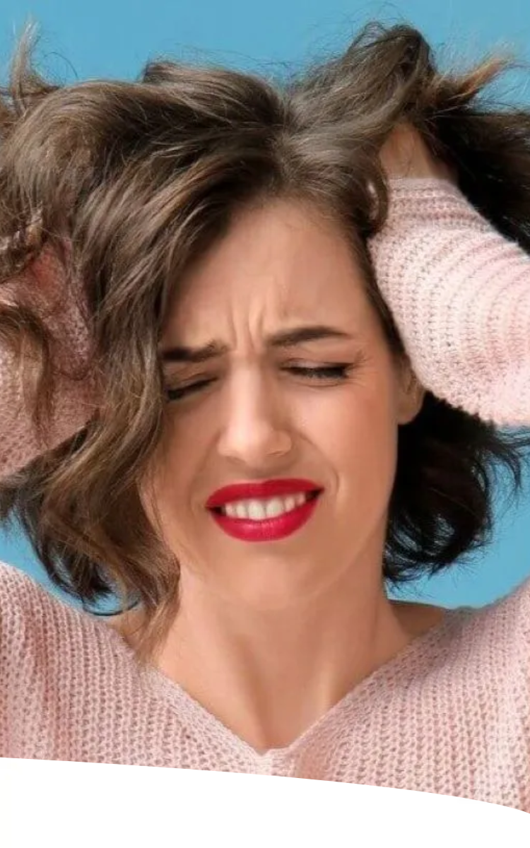 Mulher de cabelos cacheados e blusa rosa, com os olhos fechados e dentes cerrados, segurando a cabeça com as mãos em um gesto de estresse, sobre fundo azul.