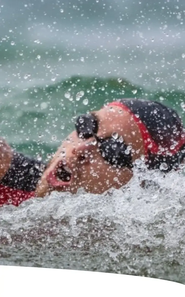 Atleta nadando em mar aberto durante etapa de natação do triatlo Ironman.
