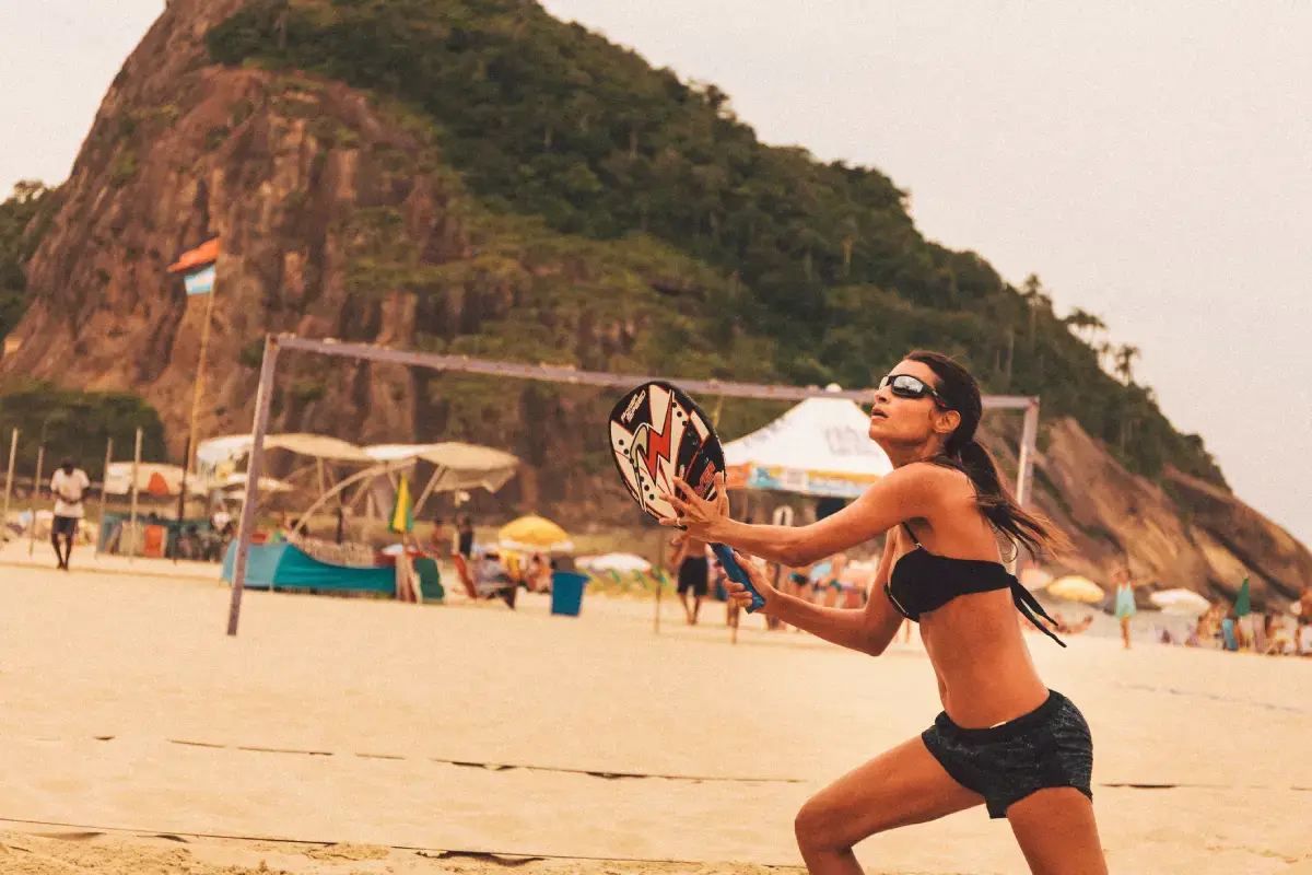Mulher jogando beach tennis, com óculos e roupas apropriadas, na praia, no Rio de Janeiro.
