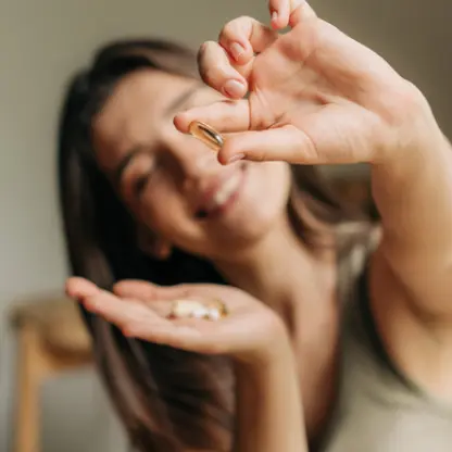 Mulher sorrindo enquanto segura cápsulas de vitaminas na mão, representando dúvidas e curiosidades sobre suplementos e ganho de peso.