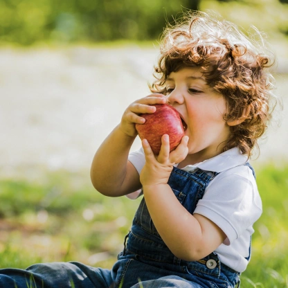 Criança segurando e mordendo uma maçã ao ar livre, representando alimentação saudável para fortalecer a imunidade durante viagens.
