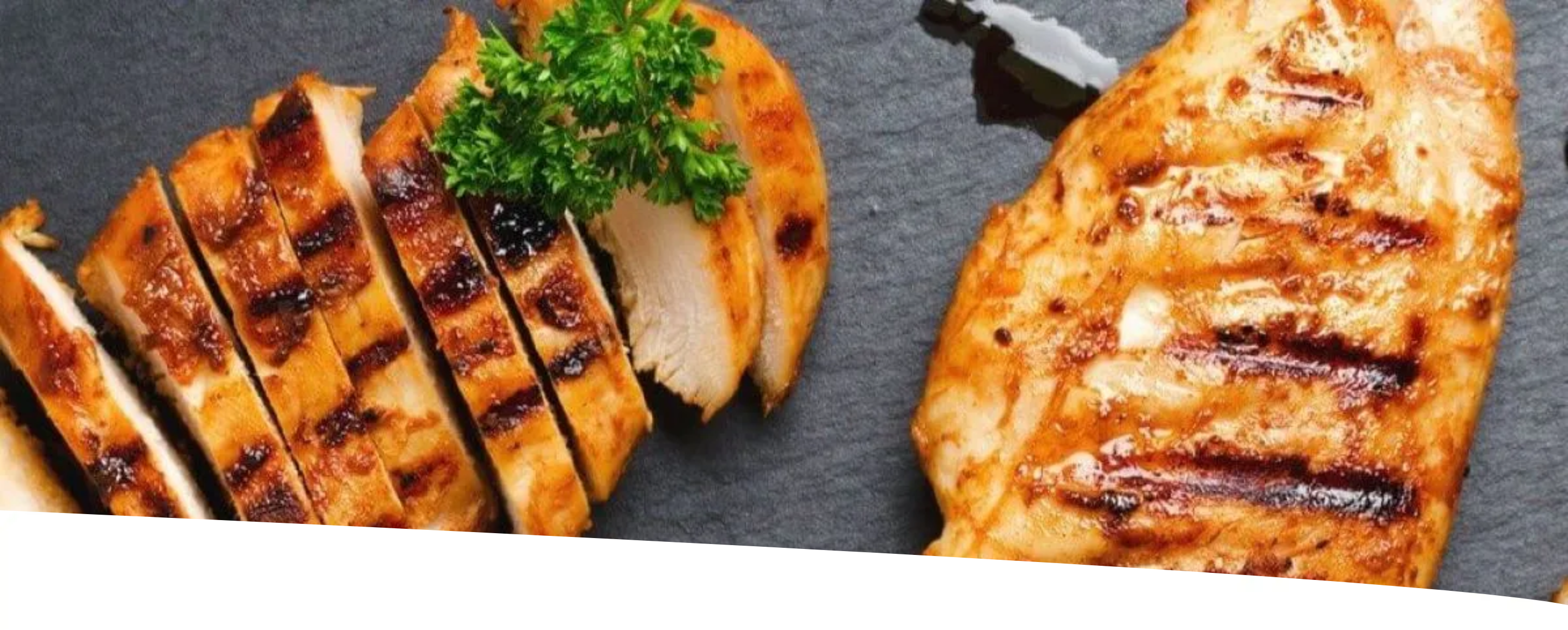Peito de frango grelhado fatiado em uma tábua escura, decorado com ervas.