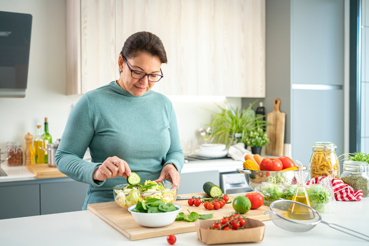 Mulher madura preparando uma salada com pepino, folhas, tomates e outros vegetais na cozinha de casa