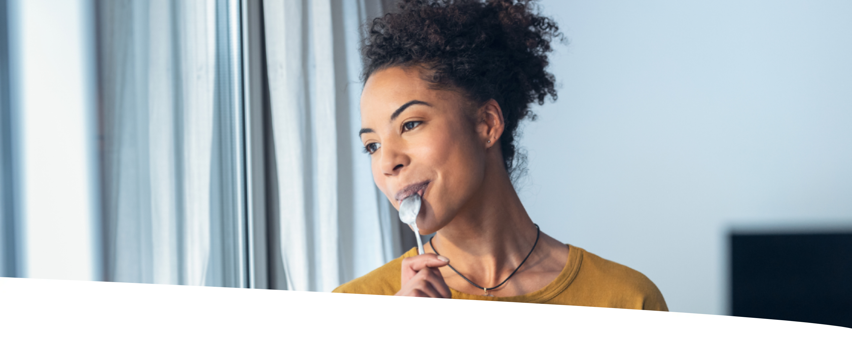 Mulher comendo cereal enquanto olha pela janela da sala.
