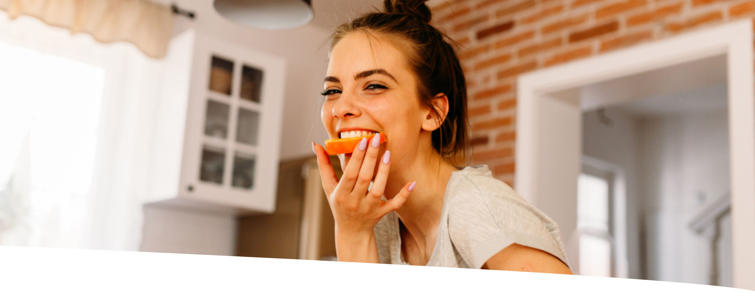 Mulher sorridente comendo metade de uma rodela de laranja.