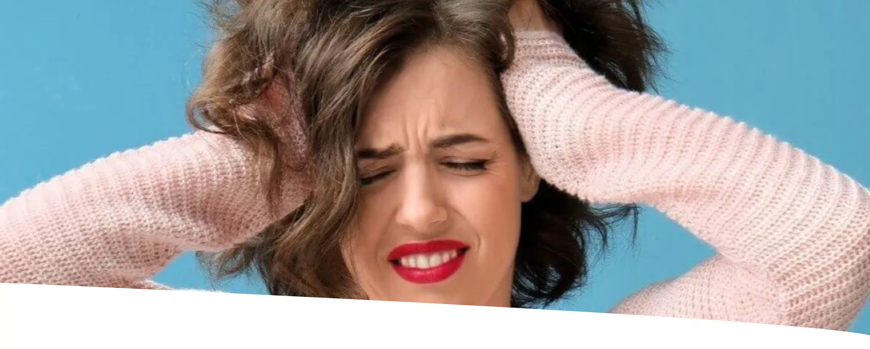 Mulher de cabelos cacheados e blusa rosa, com os olhos fechados e dentes cerrados, segurando a cabeça com as mãos em um gesto de estresse, sobre fundo azul.