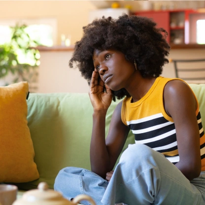 Mulher sentada no sofá com expressão cansada, ilustrando desconforto e falta de disposição comuns durante a TPM.