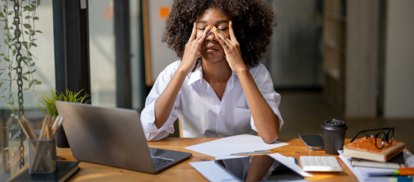 Uma mulher com as mãos no rosto, sentada em sua estação de trabalho, parece estar exausta.