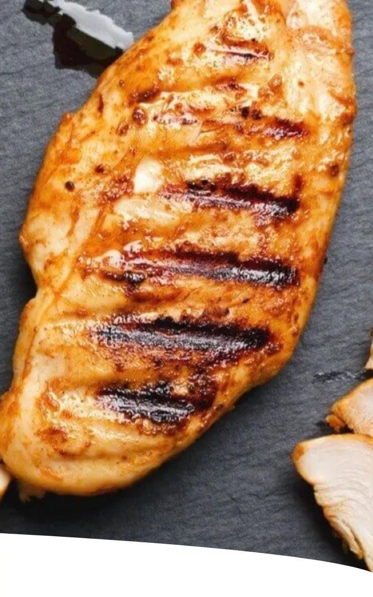 Peito de frango grelhado fatiado em uma tábua escura, decorado com ervas.