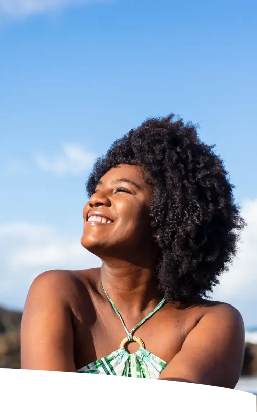 Mulher sentada em pedras, em uma linda praia, em dia ensolarado.
