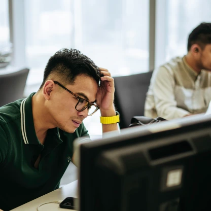 Homem sentado em frente ao computador com expressão de cansaço, ilustrando sinais de estresse no ambiente de trabalho.