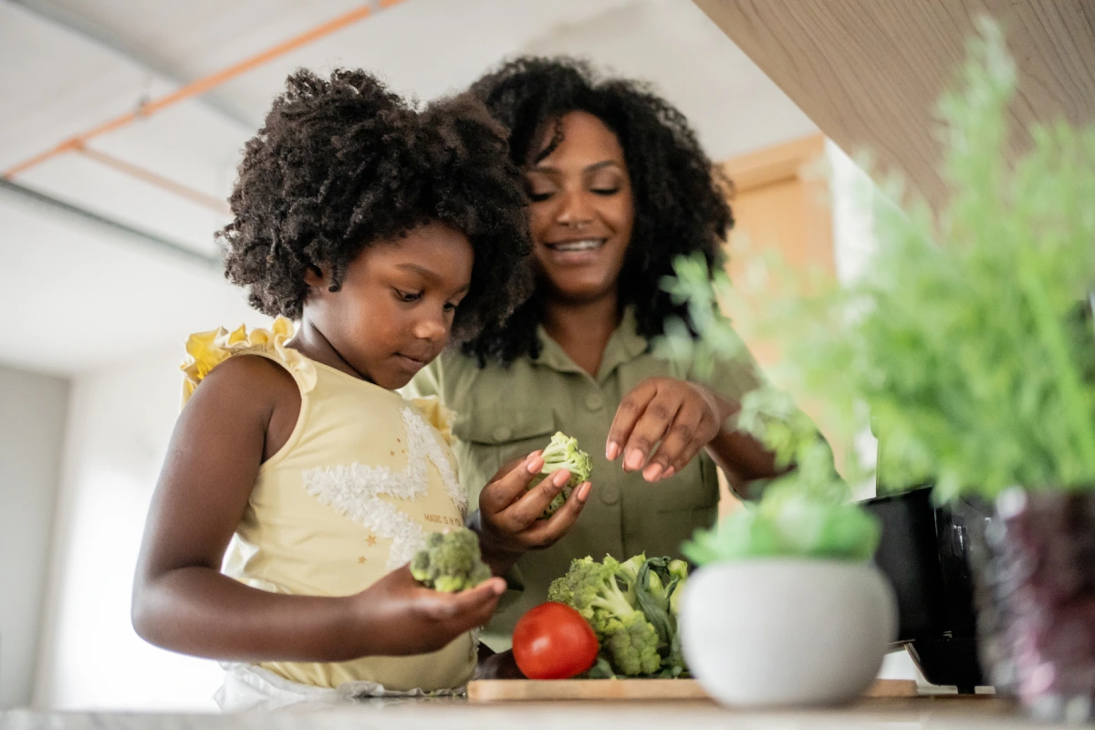 Mãe e filha estão na cozinha, separando partes de brócolis para preparar algo