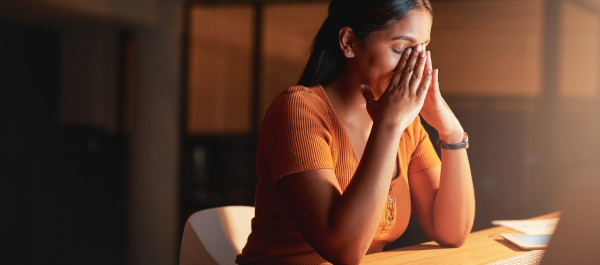 Mulher trabalhando em ambiente escuro, com as mãos no rosto