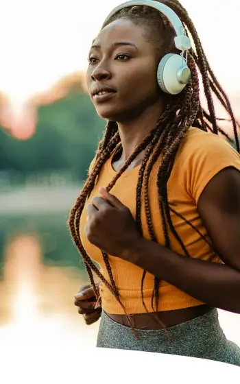 Mulher correndo ao ar livre usando fones de ouvido, representando energia, disposição e bem-estar associados a nutrientes como vitamina C e arginina.