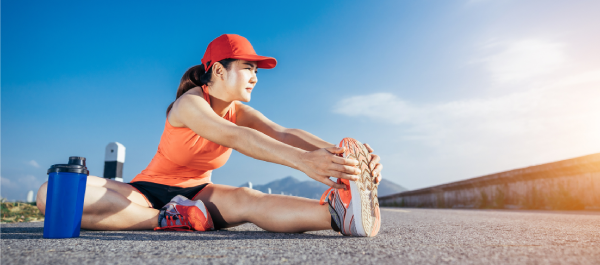 Mulher alongando a perna no asfalto, se preparando para uma corrida em uma manhã ensolarada.