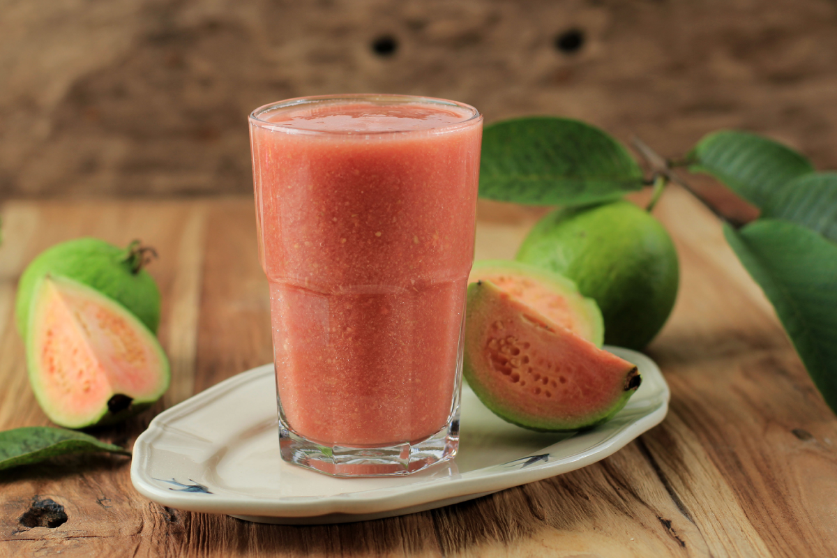 Suco de goiaba, colocado em um cenário com outras goiabas inteiras e algumas picadas.