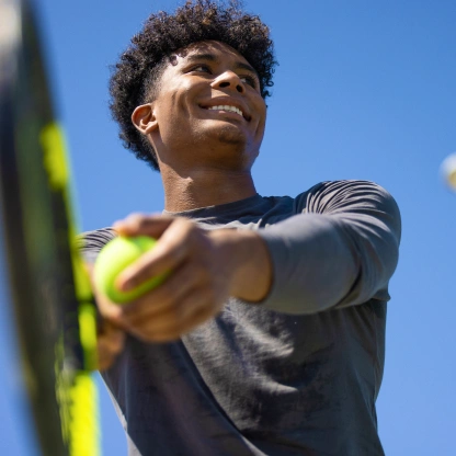 Atleta segurando uma raquete de tênis ao ar livre, ilustrando energia, foco e desempenho físico durante o treino.