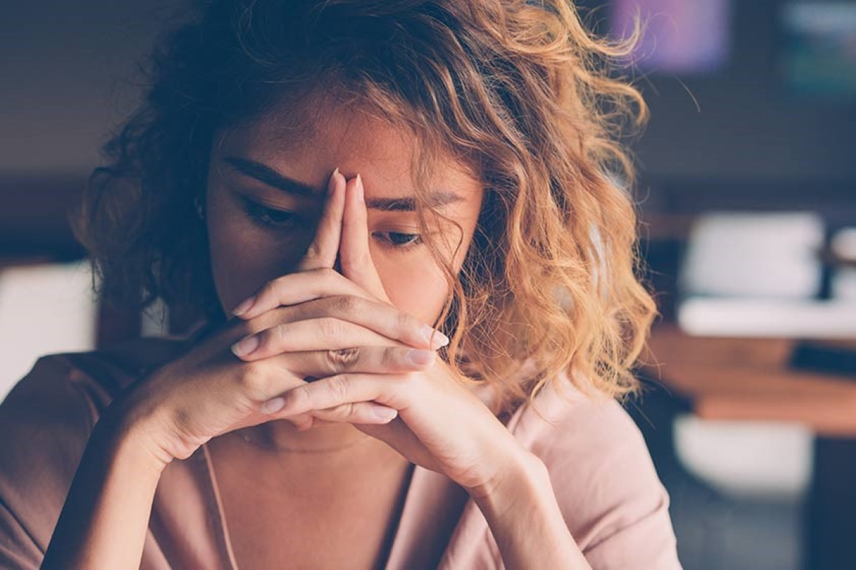 Mulher com expressão de exaustão no ambiente de trabalho, representando os sintomas de estresse e sobrecarga mental no dia a dia profissional.