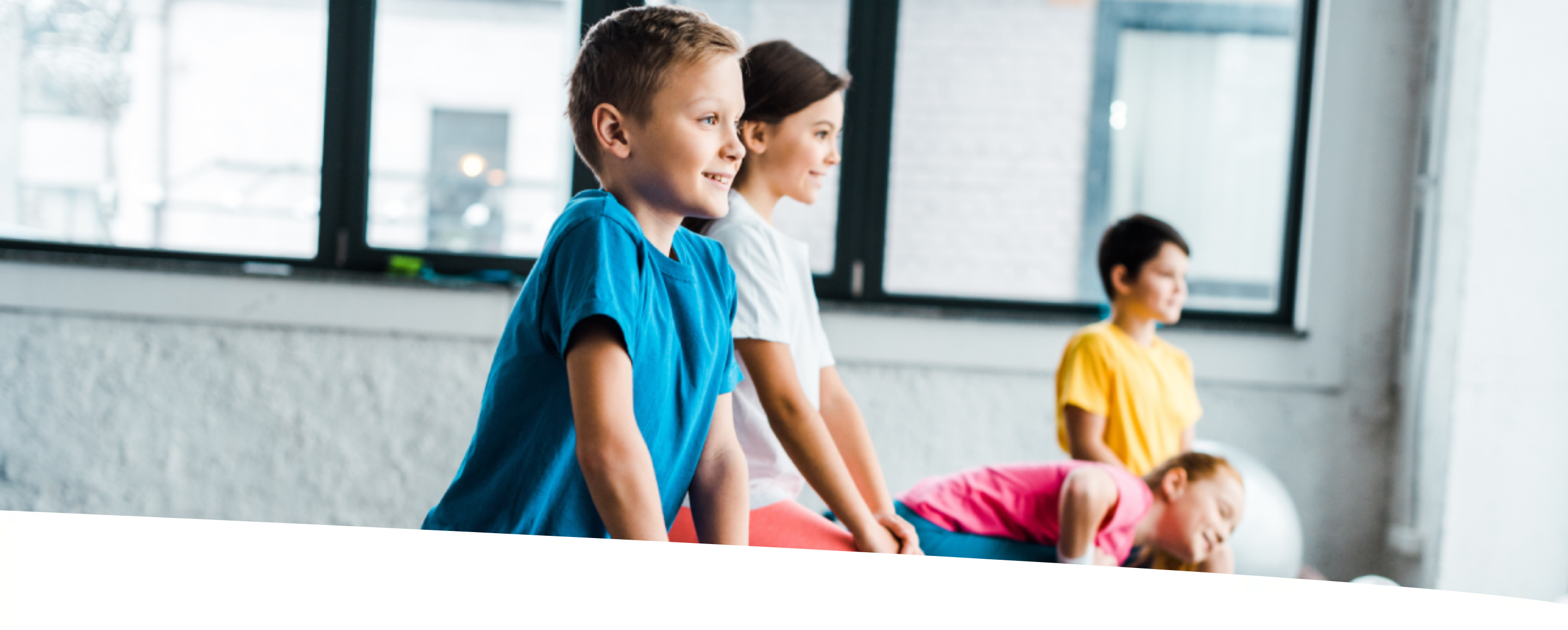 Quatro crianças fazendo alongamento em uma quadra de academia.