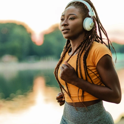 Mulher correndo ao ar livre usando fones de ouvido, representando energia, disposição e bem-estar associados a nutrientes como vitamina C e arginina.