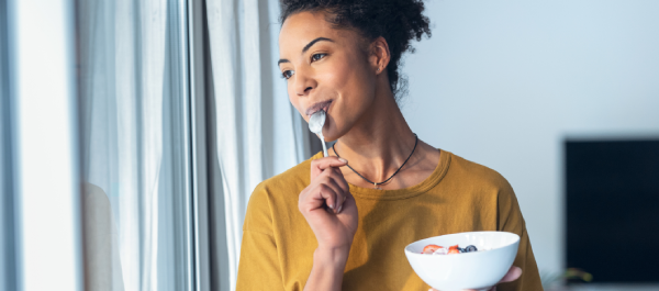 Mulher comendo cereal enquanto olha pela janela da sala.