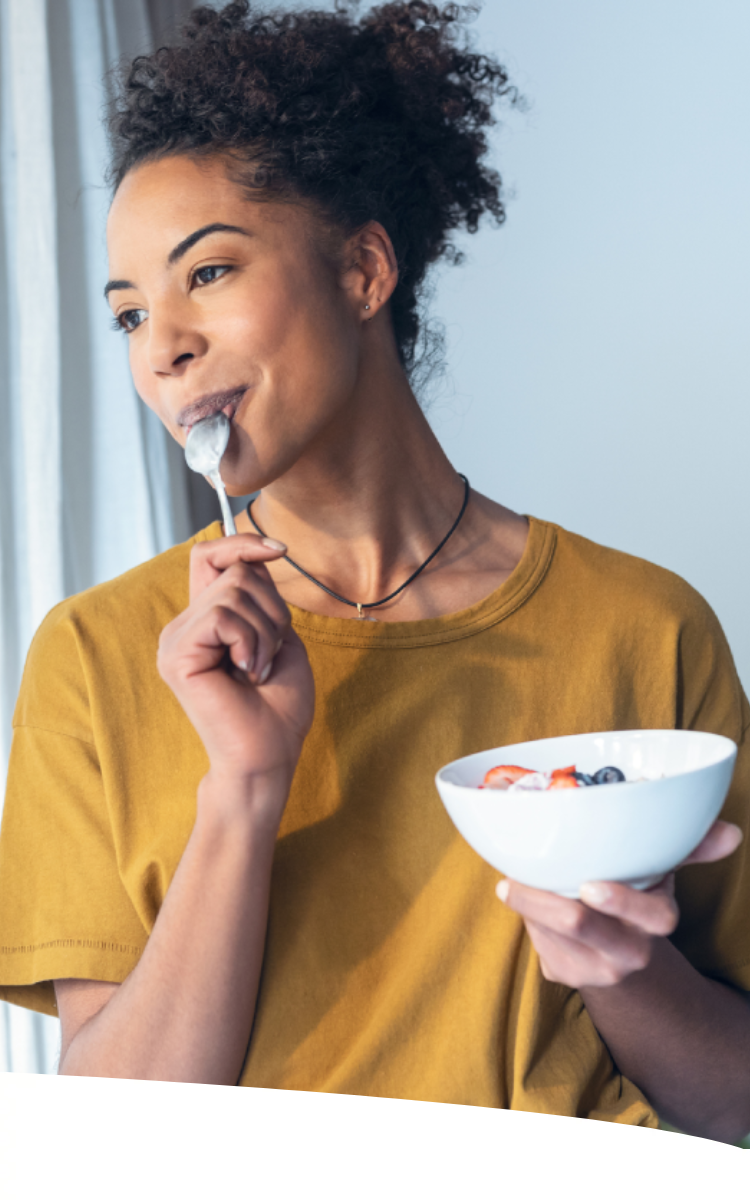 Mulher comendo cereal enquanto olha pela janela da sala.