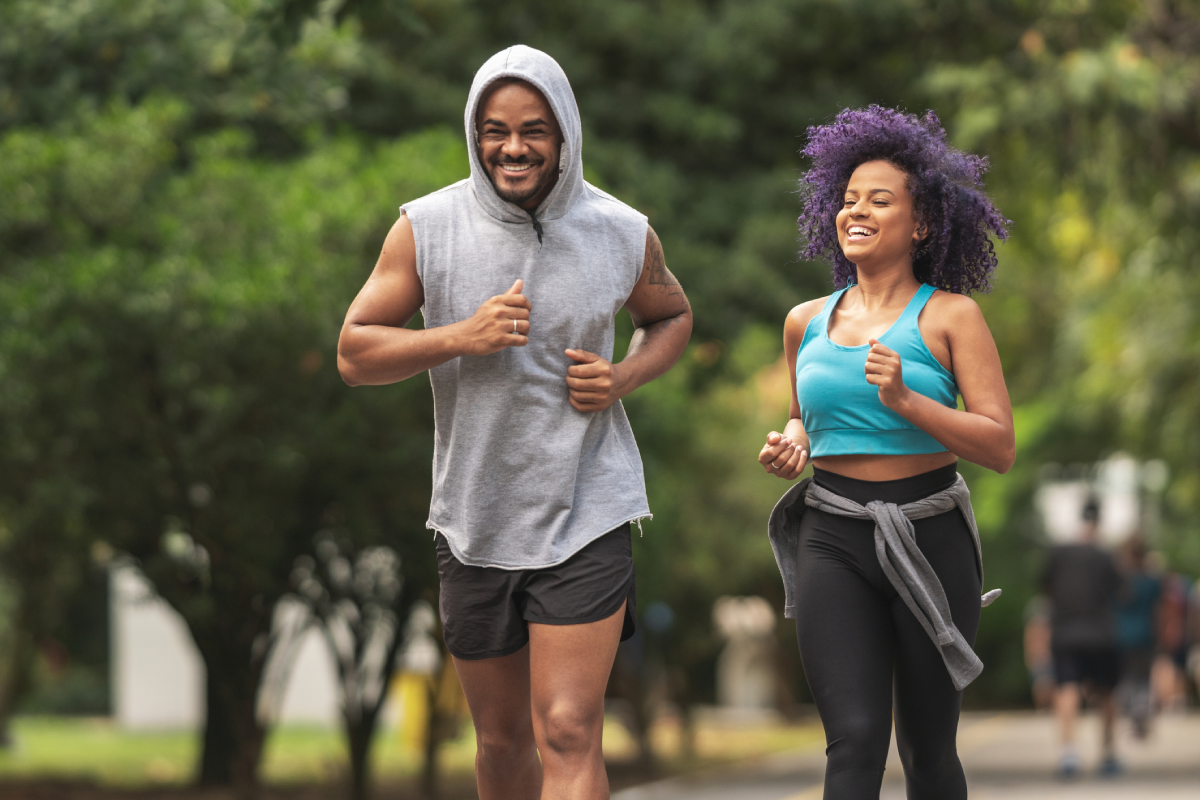 Casal correndo sorridente no parque.