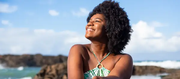 Mulher sentada em pedras, em uma linda praia, em dia ensolarado.