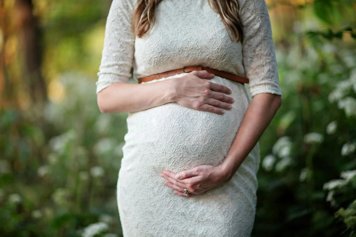 Mulher grávida em um vestido branco segurando a barriga com as mãos, transmitindo a calma e a beleza da maternidade. A imagem reflete a profunda jornada hormonal e emocional da gravidez.