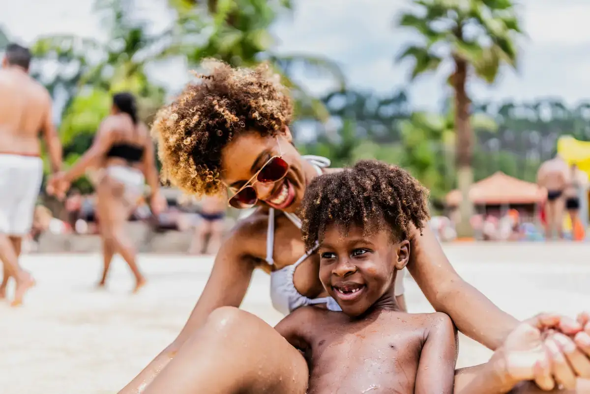 Mãe e filho sentados na areia da praia, curtindo dia ensolarado.