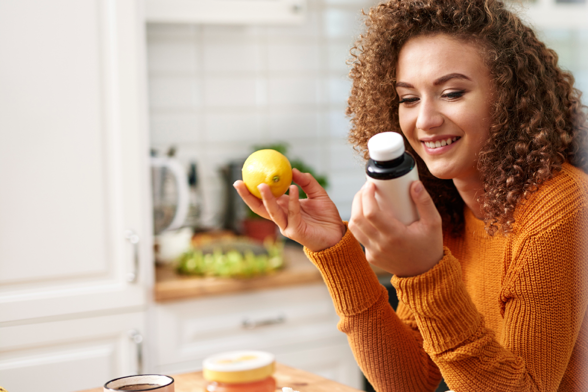 Mulher sentada a mesa com frasco de suplemento em uma das mãos